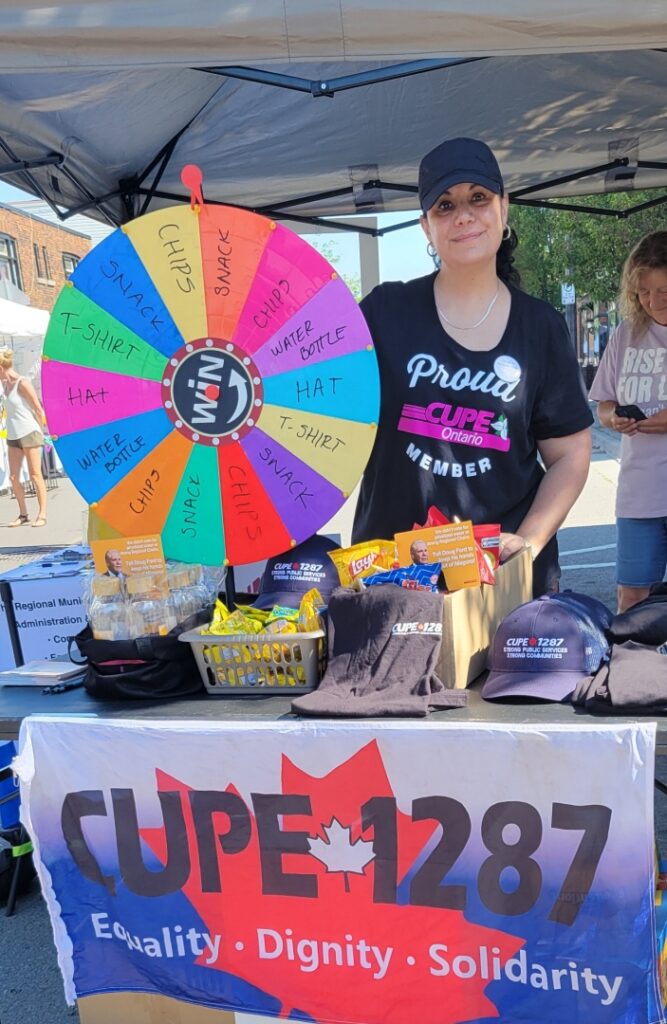 Woman wearing black hat and black t-shirt in a tent with a rainbow prize wheel